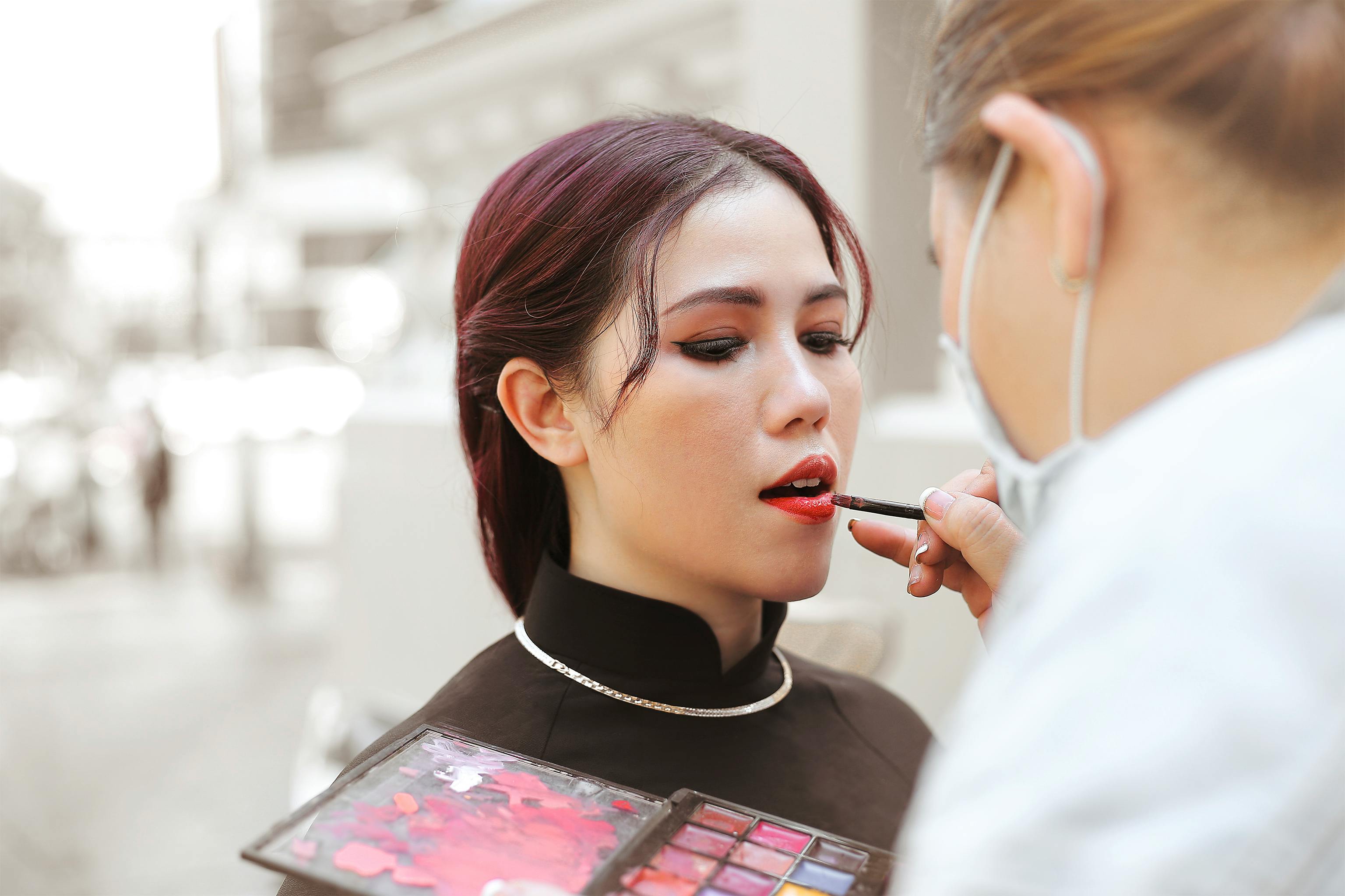 Woman receives expert makeup application outdoors with vibrant lipstick.