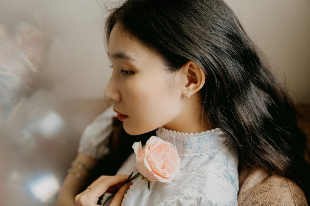 A serene portrait of a woman holding a pink rose, highlighting delicate beauty and elegance.